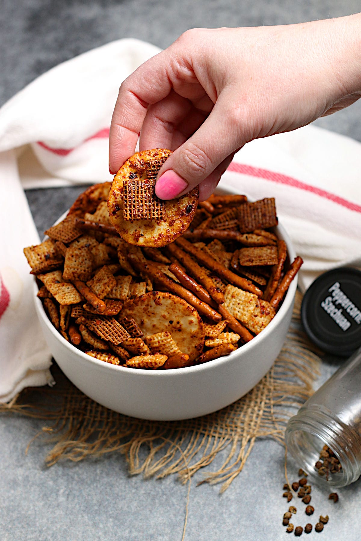 A hand grabbing some Spicy Sichuan Chex Mix from a white bowl.