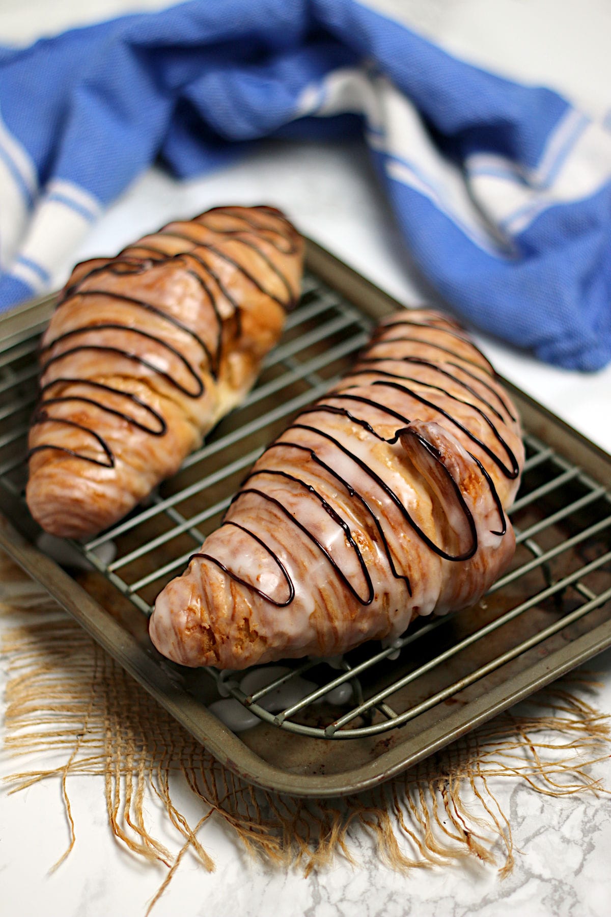 Two chocolate drizzled Glazed Croissants on a small baking sheet.