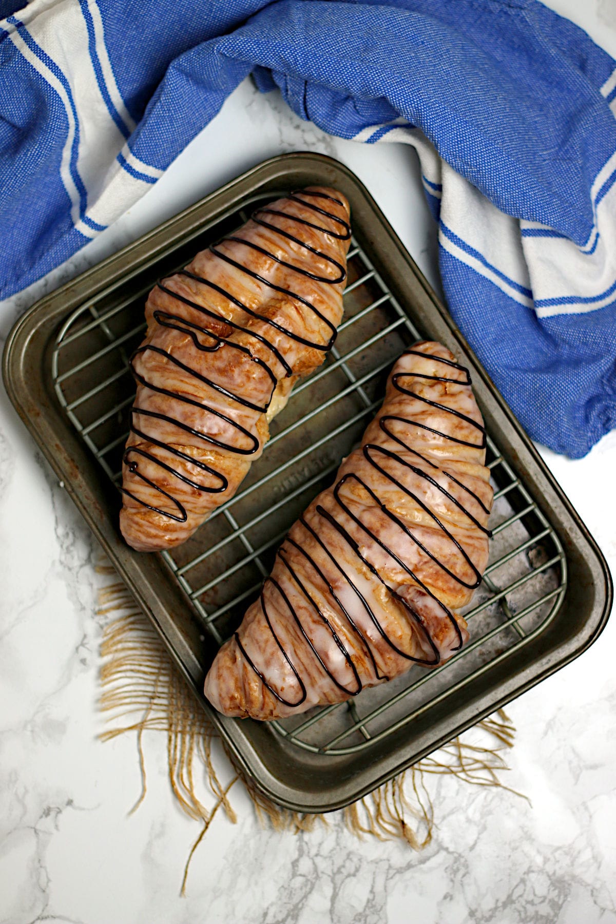 An overhead photo of two chocolate drizzled Glazed Croissants on a small baking sheet.