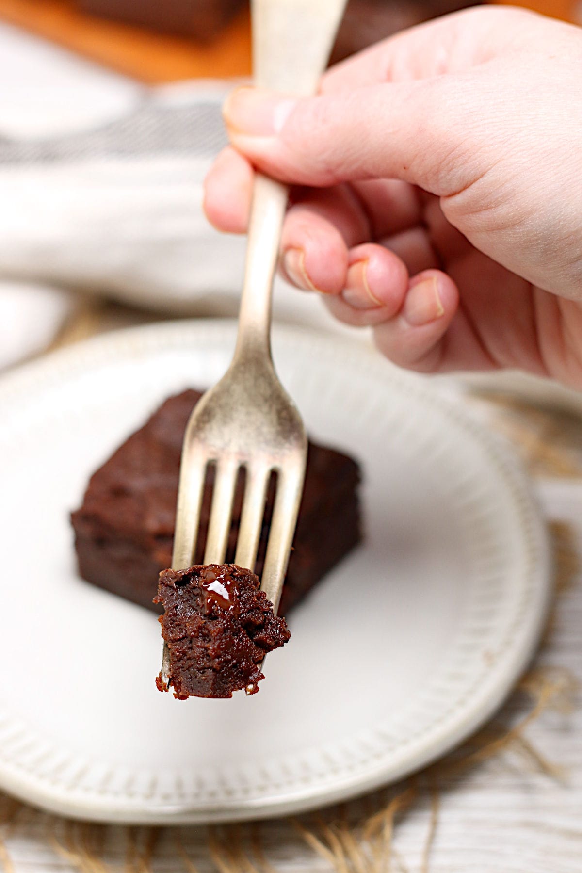 A hand holding a piece of Mocha Fudge Vegan Brownie on a fork.