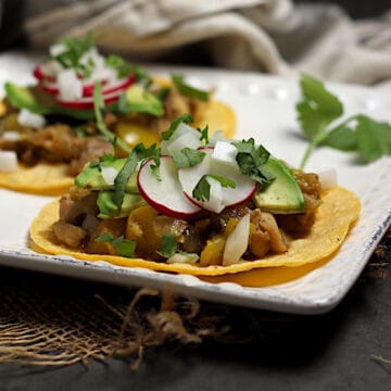 Two Green Chile Chicken tacos on a square white plate.