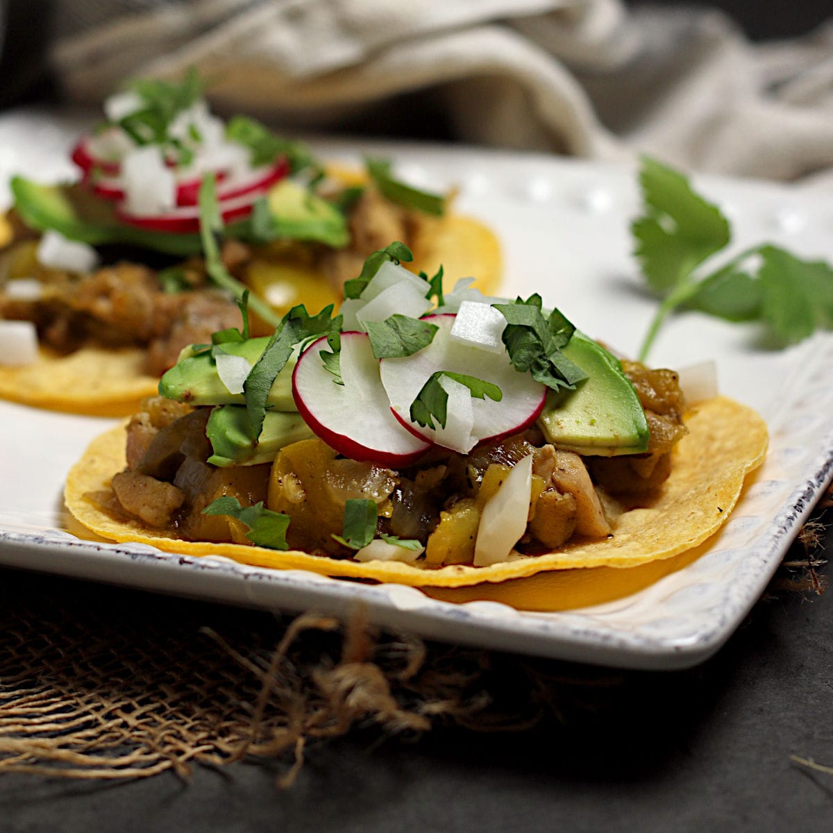Two Green Chile Chicken tacos on a square white plate.