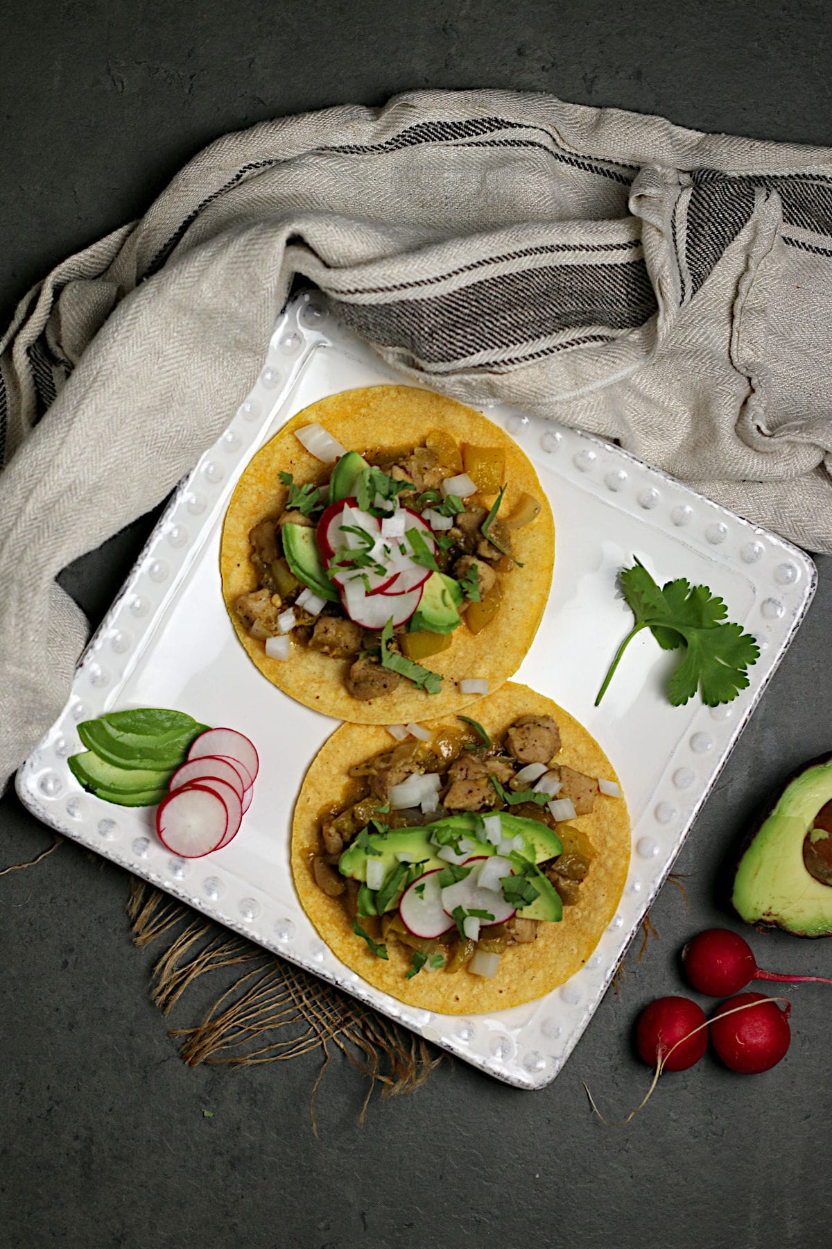 An overhead photo of two Green Chile Chicken tacos on a square white plate.
