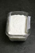 Homemade queso fresco pressed into a glass container lined with a strip of parchment paper.