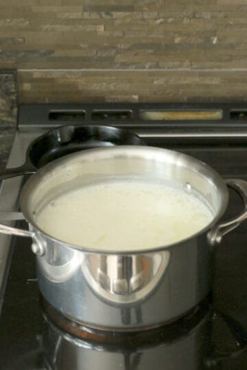 Curdled milk to make queso fresco in a saucepan on a stove.
