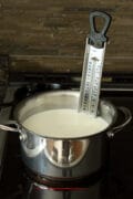 Milk heating on the stove in a saucepan fitted with a candy thermometer.