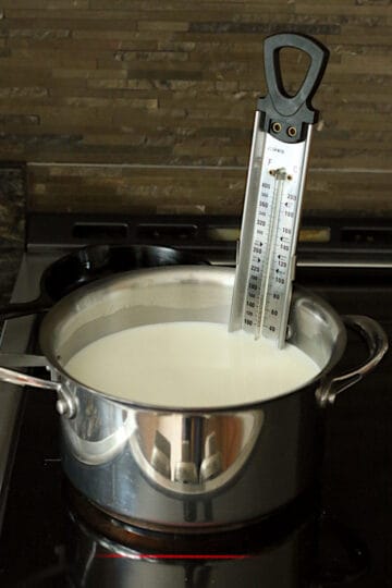 Milk heating on the stove in a saucepan fitted with a candy thermometer.