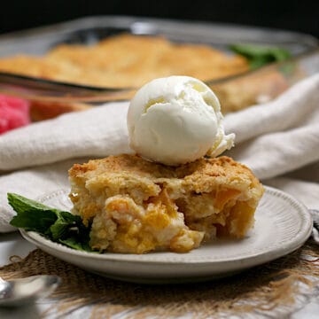 Peaches and Cream Cobbler topped with a scoop of vanilla ice cream on a small white plate.