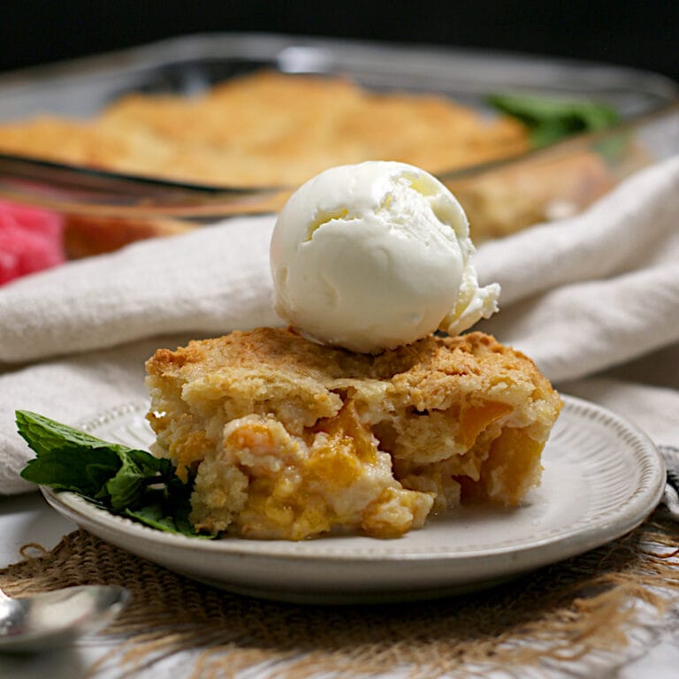 Peaches and Cream Cobbler topped with a scoop of vanilla ice cream on a small white plate.