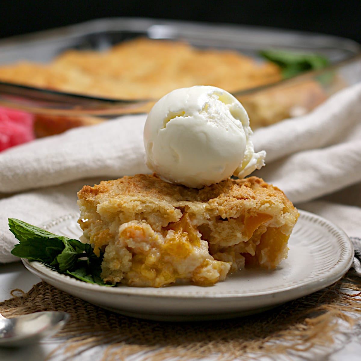 Peaches and Cream Cobbler topped with a scoop of vanilla ice cream on a small white plate.