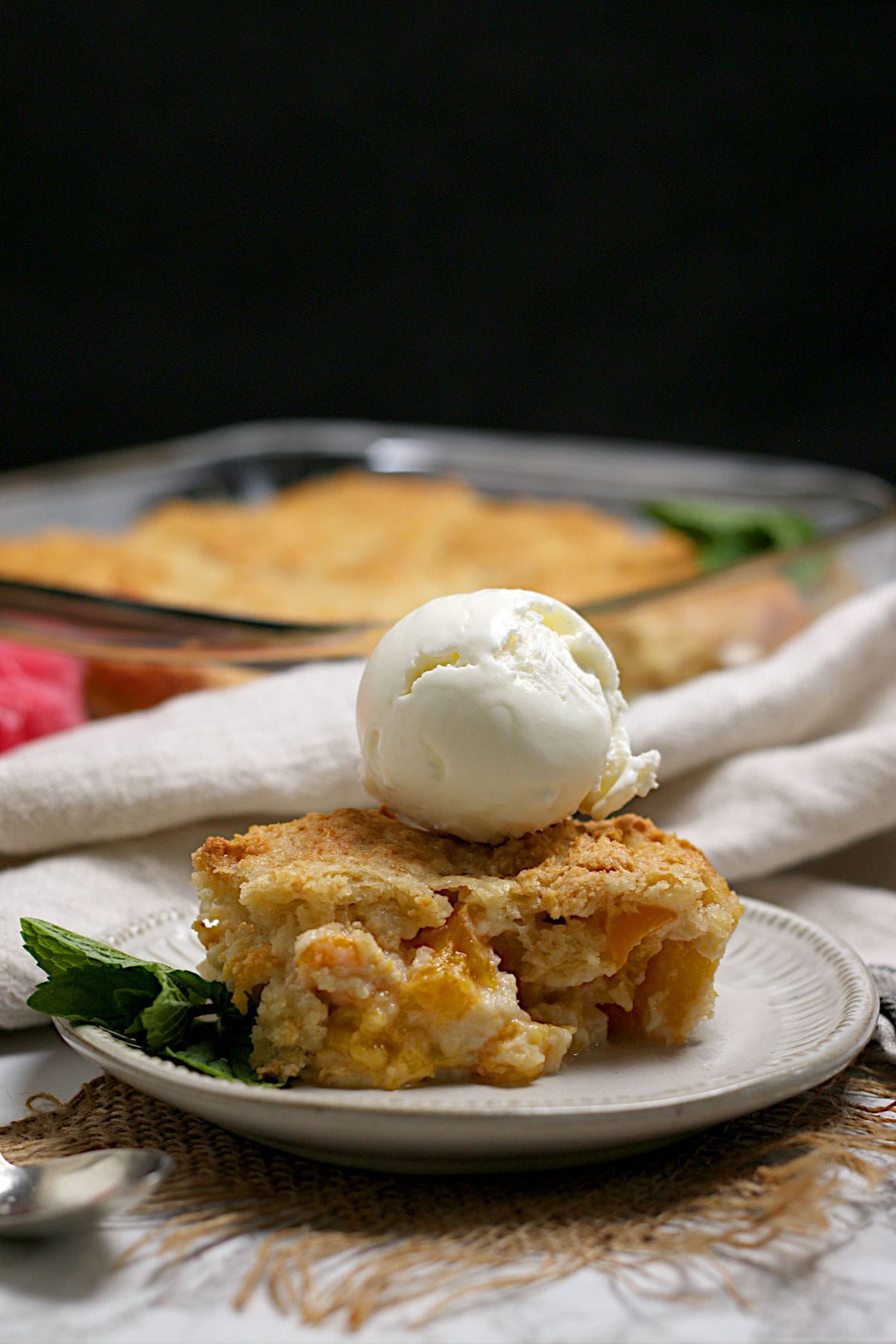 Peaches and Cream Cobbler topped with a scoop of vanilla ice cream on a small white plate.