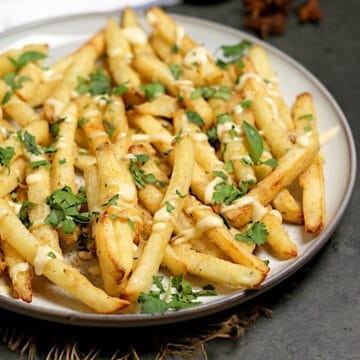 Pho-Inspired Fries (Phries) A plate full of Pho-Inspired Fries topped with lime mayo and chopped herbs.