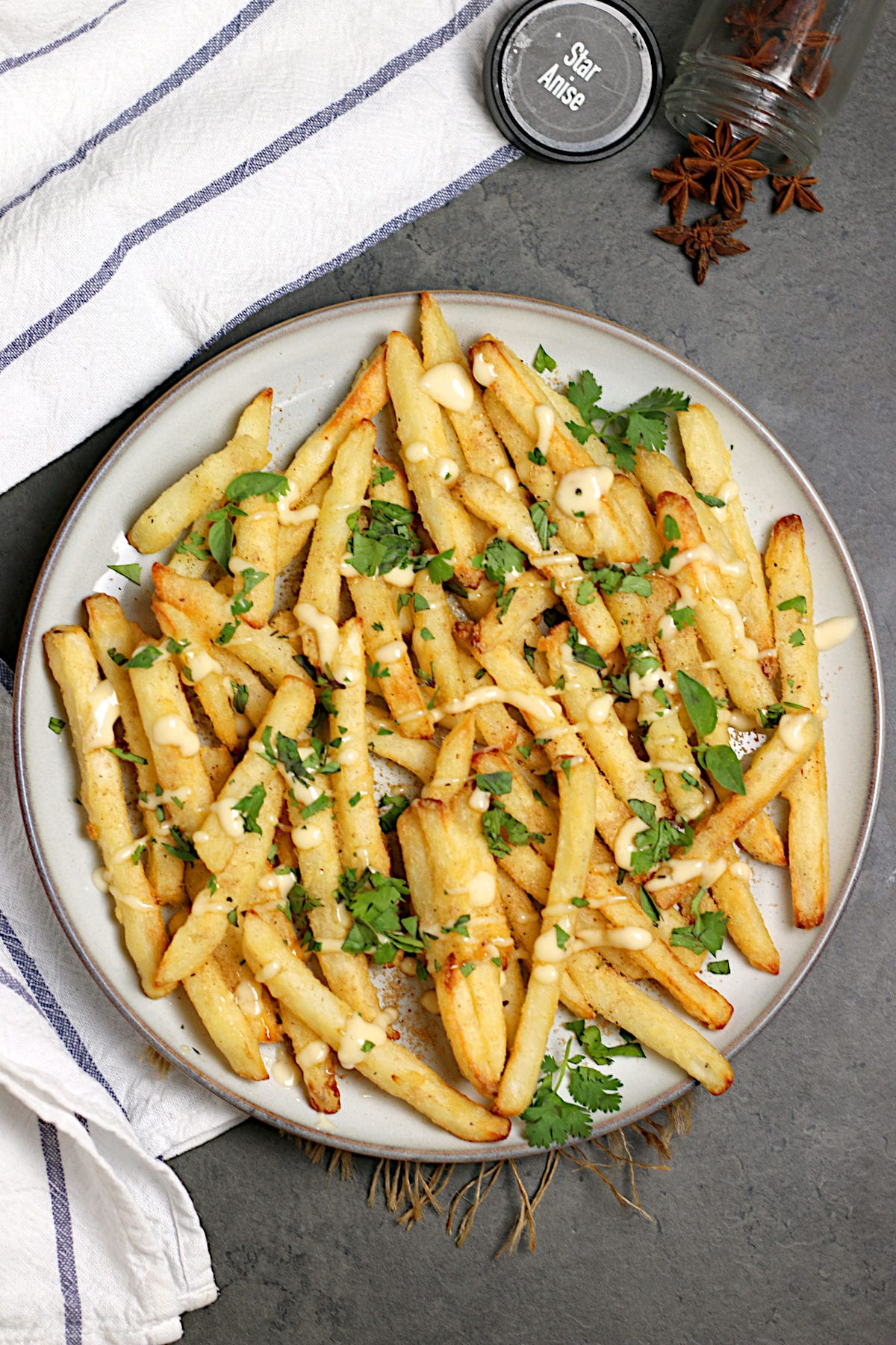 Pho-Inspired Fries (Phries) An overhead photo of a plate full of Pho-Inspired Fries topped with lime mayo and chopped herbs.