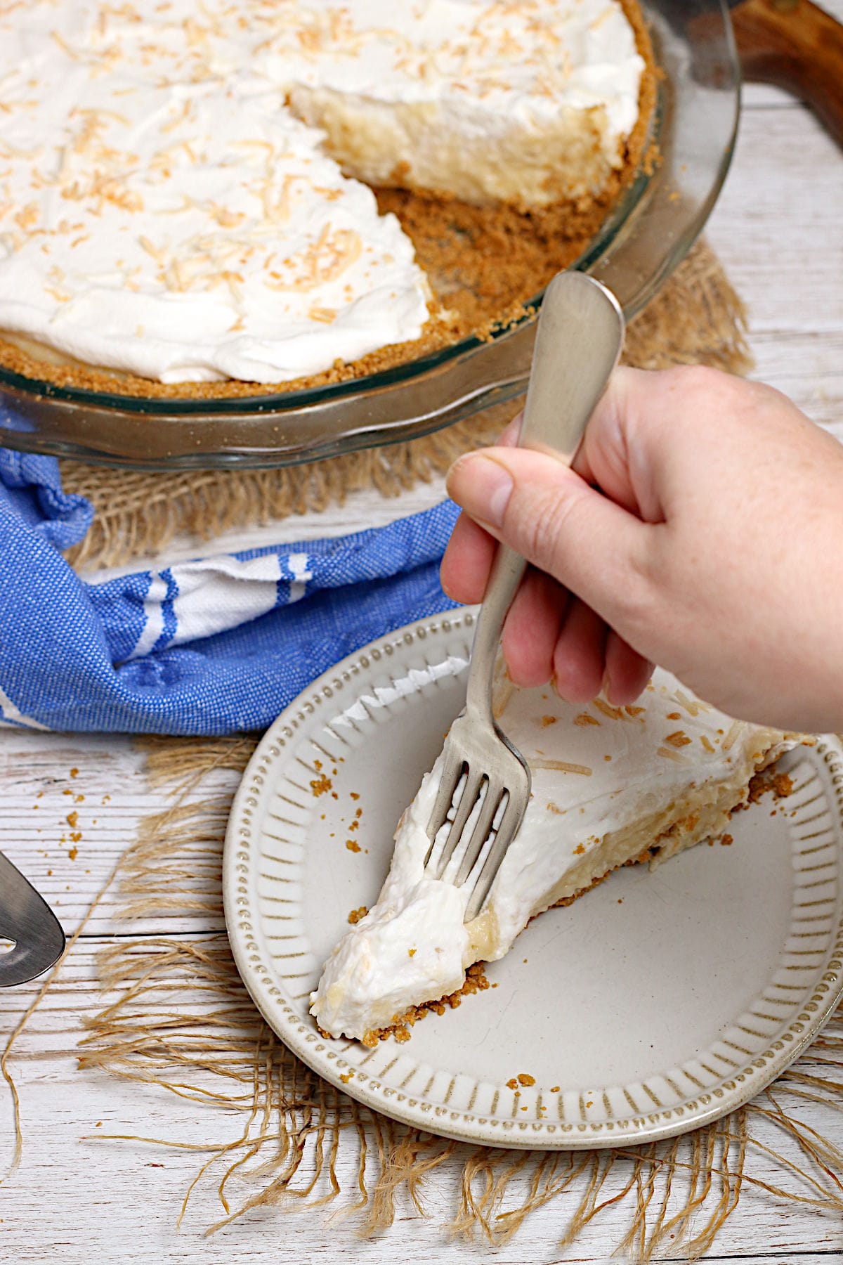 Coconut Cream Pie A hand scooping a forkful of Coconut Cream Pie from a small white plate.