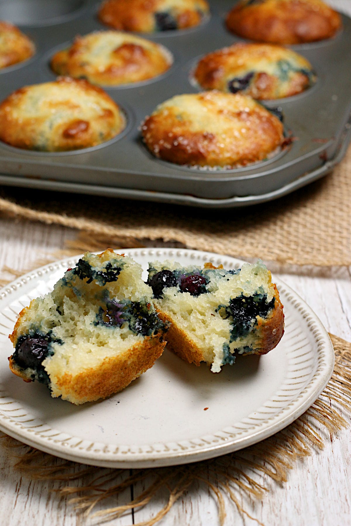 Blueberry Greek Yogurt Muffins A Blueberry Greek Yogurt Muffin broken into two pieces on a small white plate.