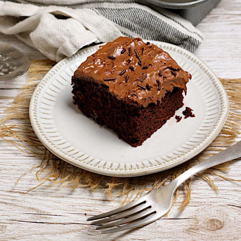 A slice of chocolate cake frosted with Easy Copycat Deep 'n Delicious Frosting on a small white plate.