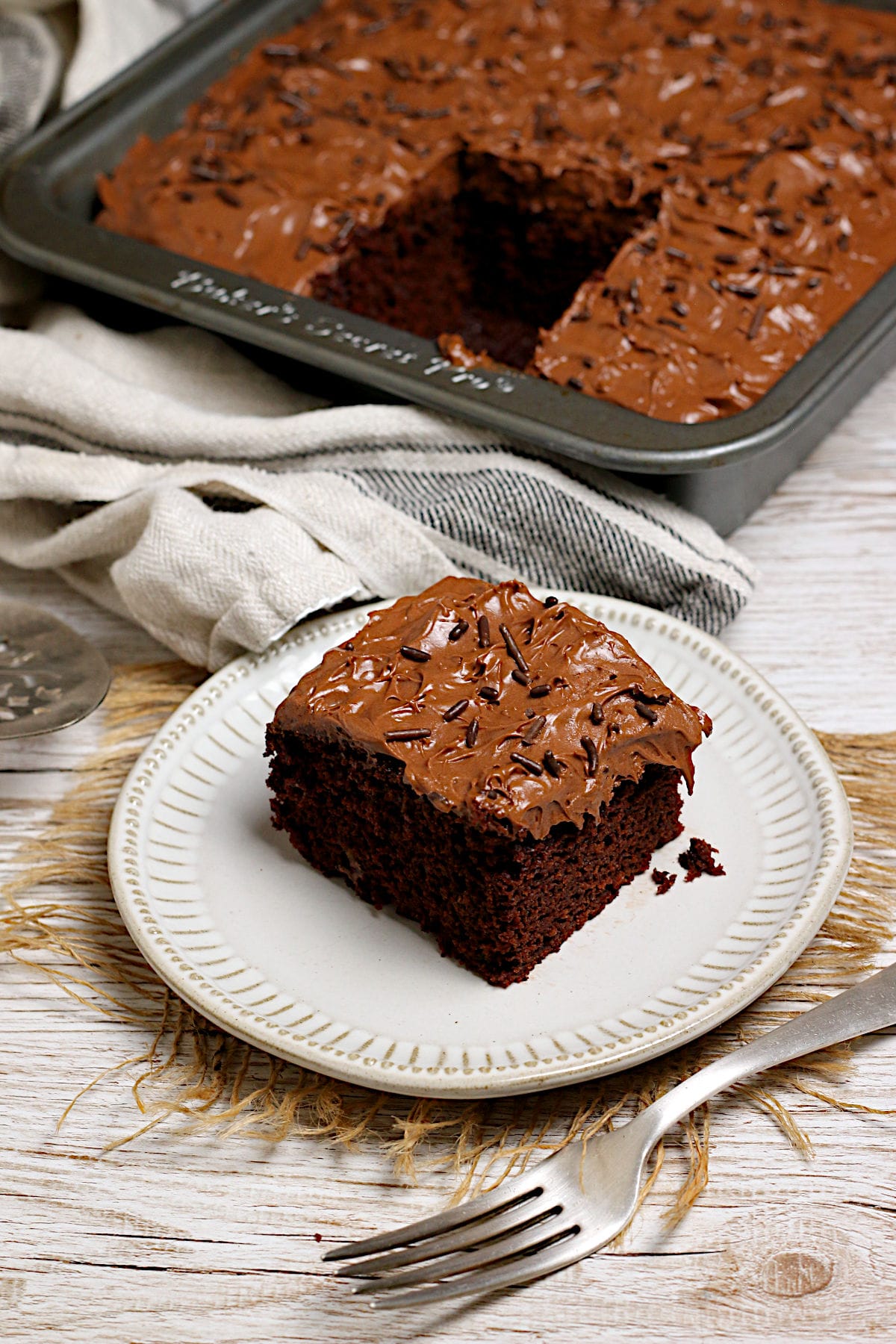Easy Copycat Deep 'n Delicious Cake Frosting A slice of chocolate cake frosted with Easy Copycat Deep 'n Delicious Frosting on a small white plate.
