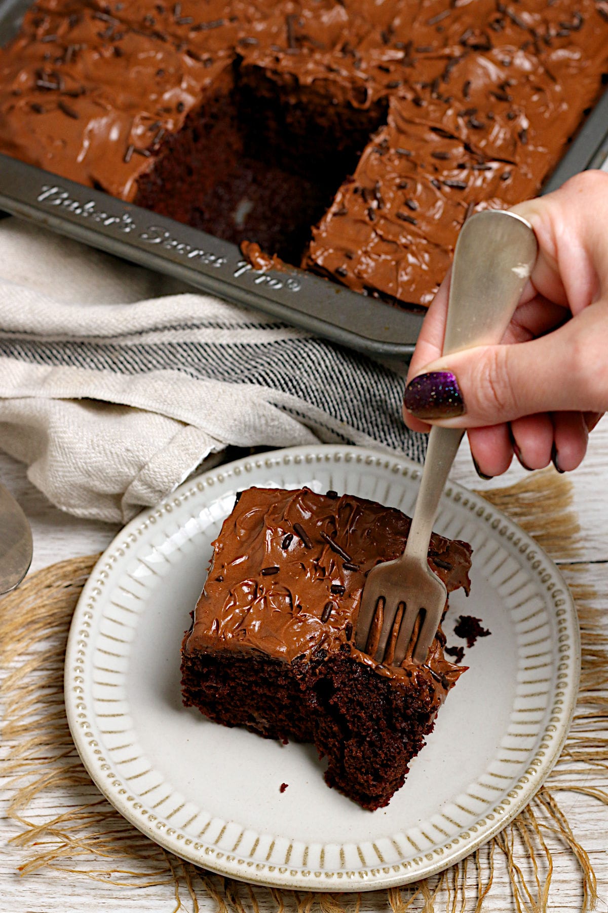 Easy Copycat Deep 'n Delicious Cake Frosting A fork taking a scoop of chocolate cake frosted with Easy Copycat Deep 'n Delicious Frosting from a small white plate.